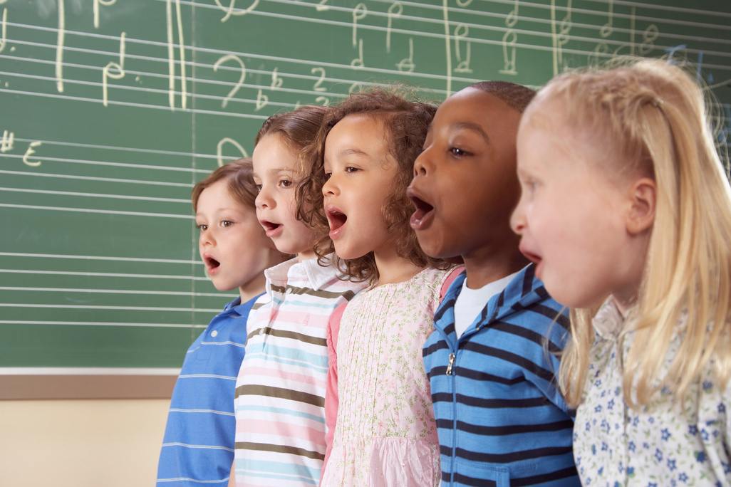Five school children (5-10) singing in class, close-up